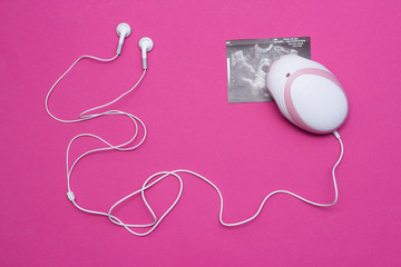Fetal doppler with headphones for listening to the baby s heartbeat in pregnant women and a picture of the ultrasound of pregnancy, close-up, pink background