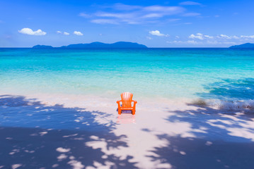 Fototapeta na wymiar Orange plastic chair on pebble beach, beautiful blue sky and sea, island in background