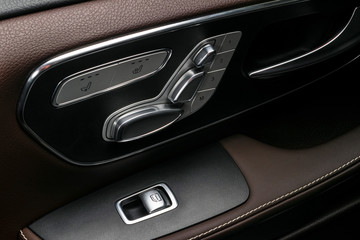 Door handle with Power window and seat control buttons of a luxury car. Brown perforated leather interior with white stitching of the luxury modern car. Modern car interior details. Car detailing