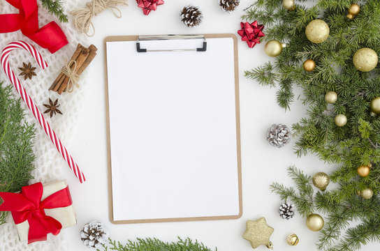 Trendy Christmas Mockup. Xmas new year composition clipboard with blank paper sheet, pine cones fir branches, gift box, golden balls, candy on white background. Flat lay, top view