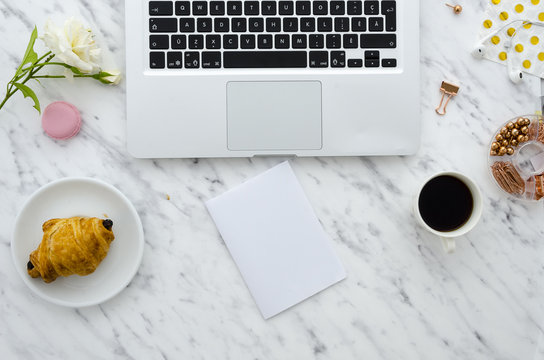 Flat lay hero header on marble background with laptop, croissant and office supplies. Mock up, copy space