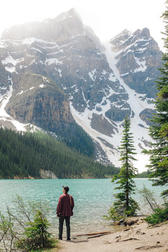 Young Man Gazing Out Onto a Beautiful Blue Lake Surrounded by Snowy Mountain Peaks