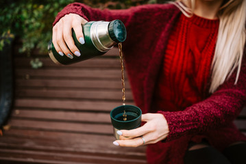 Traveler girl pouring tea from thermos cup, outdoors. Young woman drinking tea at cup. Woman pouring a drink in mug from thermos. Girl drinking tea during hike