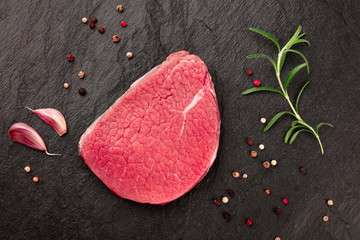 A photo of a steak of eye round beef, a raw cut, with rosemary, garlic, and pepper, shot from above...
