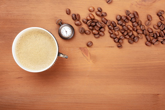 Coffee Time, vintage style. A photo of coffee in a retro cup, shot from above on a rustic wooden background with an old watch, roasted coffee beans, and a place for text