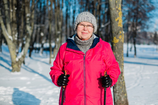 Senior woman standing with nordic walking poles in winter  park. Healthy lifestyle concept. Mature woman resting after exercise outdoors.