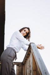 Fototapeta premium Fashion portrait of a beautiful girl near on the steps of a wooden house by the lake. Posing and resting at sunset. Emotional portrait of a girl