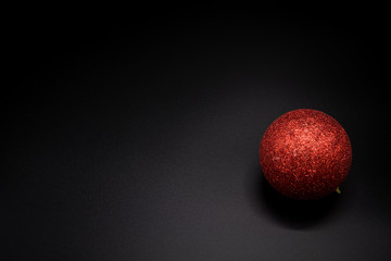 Red glittered christmas ball on black background. Copy scape.