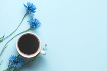 Spring background. Cornflowers and a cup of hot coffee on a wooden, blue background. Copy space