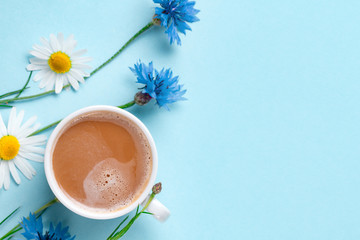 Obraz na płótnie Canvas Spring background. Cornflowers, chamomile and a cup of hot coffee on a blue background. Top view. Copy space