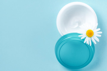 Moisturizing hand cream for dry skin and chamomile flower on a blue background. Skin care. Copy space