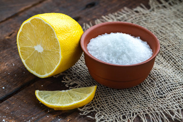 Lemon acid in a brown, small plate, a slice of lemon and a juicy lemon on a wooden background....
