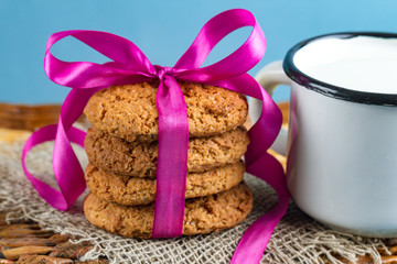 Mug of fresh milk and oatmeal cookies wrapped in a satin, pink ribbon on a blue background