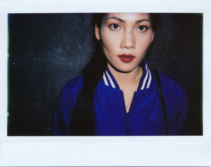 Instant wide polaroid photo of a beautiful Asian woman in blue bomber jacket