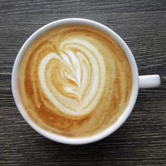 Fototapeten Top view of a mug of latte art coffee on black background. © tanarch