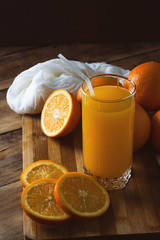 A glass of orange juice, cut into pieces Orange, Oranges on a wooden board, dark background. Beautiful Game of Light and Shadows