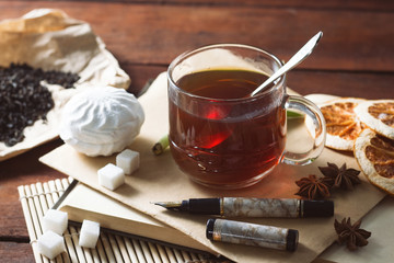 A cup of hot tea, Spices, Sweets, Envelope with pen on a wooden table