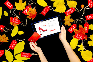 Woman female adult hands with tablet choosing fashion new red high heels with sale or discount and purchasing buying in internet online shop store in black friday holiday with autumn yellow leaves