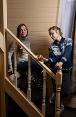 Two young women decorate with garlands a wooden staircase in the house. Preparing for the holiday.