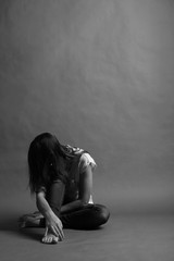 Teenager girl with depression sitting alone on the floor in the dark room. Black and white...