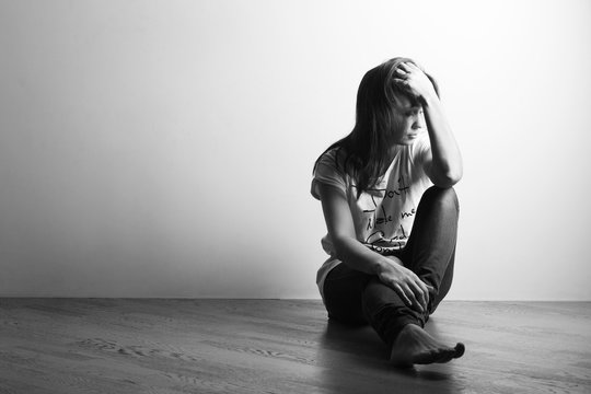 Teenager girl with depression sitting alone on the floor in the dark room. Black and white photography
