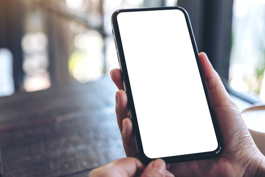 Mockup image of hands holding black mobile phone with blank white screen in vintage cafe