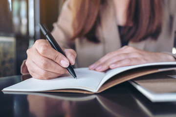 Closeup image of a business woman writing on blank notebook on wooden table