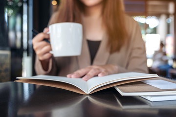Closeup image of a woman reading and opening a book while drinking coffee in cafe