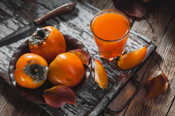 Ripe orange persimmon fruit and persimmon leaves in a brown plate on a brown wooden table