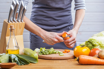 The hands of a woman cook prepare a salad with fresh vegetables.