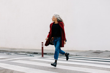 Mature woman with grey long hair crossing the street.