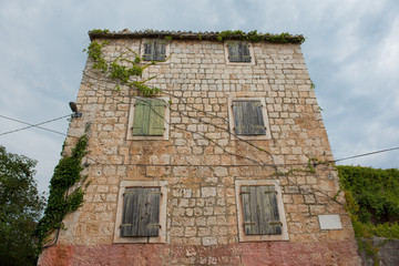 Old and abandoned house made out of stone with closed wooden windows. Blue sky with clouds in background. Vintage sea house.
