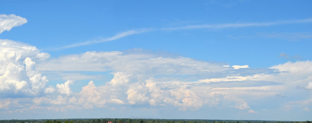 Cirrus and cumulus clouds in the sky above the field. White clouds at sunset are painted red. Calm and solid landscape