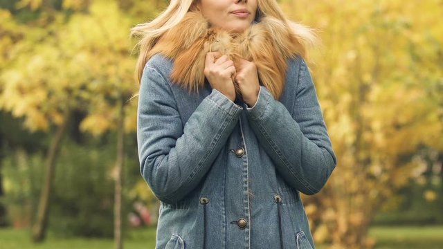 Woman waiting for friend in autumn park, shivering with cold, rubbing hands