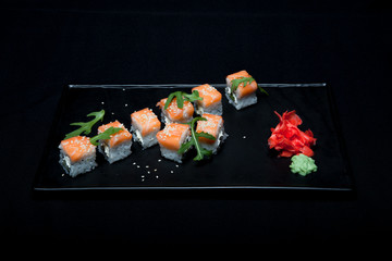 Sushi roll with salmon and avocado on plate on black background top view