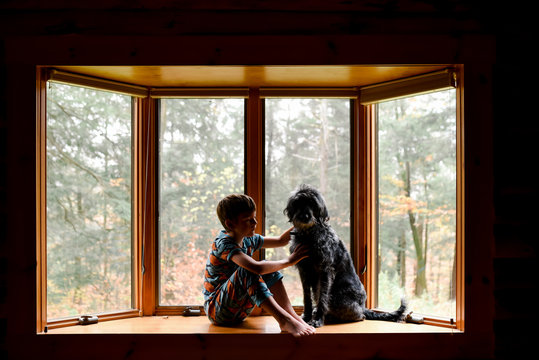 little boy sitting in a bay window with his black dog