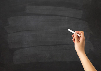 Female hand holding white chalk in front of a blank blackboard