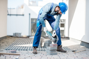 Builder in uniform cutting paving tiles with electric cutter on the construction site with white...