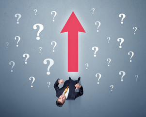 Young contemplating businessman stands in front of a big red arrow and white question marks