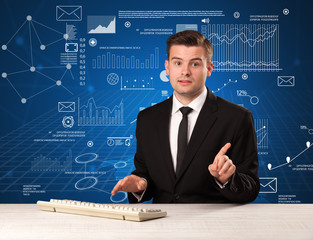 Young handsome businessman sitting at a desk with blue charts and data behind him