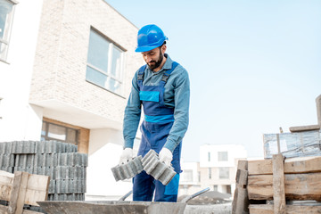 Fototapeta premium Builder loading paving tiles into the pushcart standing on the construction site