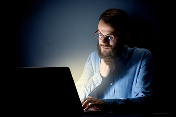Young handsome businessman working late at night in the office with a dark background
