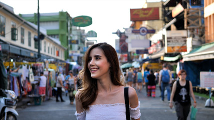 Fototapeta premium Young traveling women in city centre are walking Khaosan Road walking street in evening at Bangkok, Thailand. Happy female traveler and tourist concept.