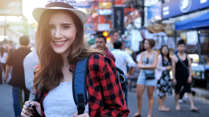 Young traveling women with backpack in city centre are walking Khaosan Road walking street in evening at Bangkok, Thailand. Happy female traveler and tourist concept.