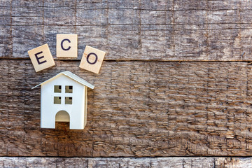 Miniature toy model house with inscription ECO letters word on wooden backdrop. Eco Village, abstract environmental background. Real estate mortgage property insurance sweet home ecology concept