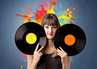 Young lady holding vinyl record on a grey background with colorful splashes behind her 