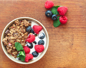 Healthy breakfast. Granola, muesli with yogurt and fresh berries in a bowl on wooden background, top view, flat lay.