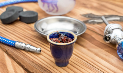 Hookah bowl with flavour tobacco and parts of hookah on wooden table.
