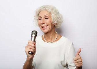 lifestyle and people concept: Portrait of charming modern grandmother holds up the microphone stand...