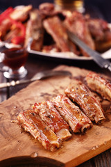 Roasted spare ribs on a wooden board with fork, knife and glass of beer on a rustic wooden table